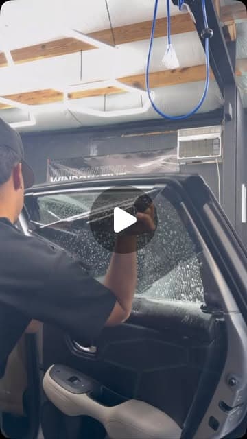 Installer squeegeeing window tint film onto a car window